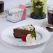 A slice of chocolate cake on a Fineline Flairware white plastic plate with a raspberry and whipped cream.
