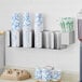 A ServSense stainless steel wall mount and countertop cup and lid holder with straw caddy attachment holding white cups with blue lines.