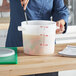 A woman using a large white Vigor food storage container to measure food in a professional kitchen.