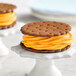 Two ice cream sandwiches with orange frosting on cookies.