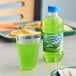 A green bottle of Hawaiian Punch Green Berry Rush next to a glass of green liquid on a table.
