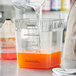 A person pouring orange juice into a Narvon slushy mix container on a counter.