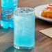 A glass of Hawaiian Punch Polar Blast blue liquid with ice on a table next to a bottle of Hawaiian Punch Polar Blast.