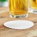 A glass of beer on a 4" white scalloped edge coaster.
