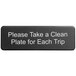 A black Tablecraft sign with white text that says "Please Take a Clean Plate for Each Trip" on a counter.