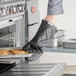 A person wearing an Outset black flame retardant oven mitt putting cookies on a tray.