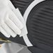 A person wearing a white glove uses a Carlisle Sparta Easy Slicer cleaning pad to clean a black object.