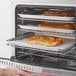 A person putting pizza trays in an Avantco countertop convection oven.