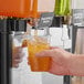 A person using Pure Craft Beverages Pineapple Papaya Beverage Concentrate to fill a plastic cup with a green liquid.
