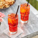 Two glasses of Pure Craft Blood Orange soda with straws on a marble table.