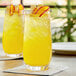 A table with two glasses of yellow Pure Craft Beverages Mango Lemonade with fruit on top.