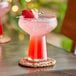 A Libbey coupe glass with a pink drink and a strawberry on a table coaster.