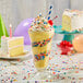 A glass with yellow Frostline birthday cake soft serve with whipped cream and sprinkles.