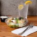 A Dart PresentaBowls clear plastic container filled with salad on a table next to a glass of water.