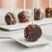 A Chalet Desserts chocolate covered cake pop with sprinkles on a white plate.