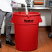 A man standing next to a red Continental 44 gallon round trash can.