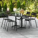 A black Lancaster Table & Seating outdoor dining table with chairs and an umbrella on a patio.