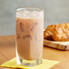A glass of Land O Lakes Cocoa Classics Chocolate Supreme Cocoa with ice on a wooden surface with a croissant.