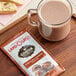 A glass mug of hot chocolate next to a Land O Lakes Cocoa Classics Chocolate Supreme cocoa mix packet.