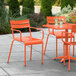 An orange Lancaster Table & Seating outdoor arm chair at an orange table on a patio.