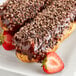 A white plate with two chocolate covered donuts, one topped with Cacao Barry cacao nibs and one topped with strawberries.