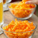 A hand holding a bowl of Good's Crunchy Cheese Curls on a table.