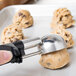 A ball of cookie dough with a Vollrath black metal scoop on top of it.