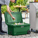 A man opening a CaterGator hunter green outdoor cooler to put a can inside on a table in a outdoor catering setup.
