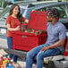 A man and woman sitting in the back of a truck with a red CaterGator outdoor cooler.