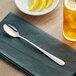 An Acopa Brigitte stainless steel iced tea spoon on a napkin next to a plate of lemon wedges.