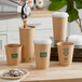 A person pouring coffee into a New Roots smooth brown paper cup with green text.