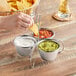 A person using a Choice stainless steel condiment server to dip a chip into guacamole.