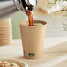 New Roots compostable paper hot cup filled with coffee on a counter being poured from a coffee pot.