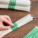 A person wrapping a napkin with a green and white checkered paper band.