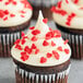 A chocolate cupcake with white frosting and Regal red heart sprinkles.