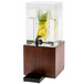 A Cal-Mil dark wood infusion beverage dispenser on a counter with lemons and limes inside.