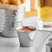 An American Metalcraft stainless steel sauce cup filled with red sauce on a table with a bucket of fried chicken.