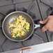 A hand using a Vollrath aluminum non-stick fry pan to cook scrambled eggs with peppers on a stove.