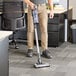 A man using a Lavex cordless stick vacuum to clean a room in a professional kitchen.