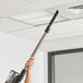 A person using a Lavex cordless stick vacuum to clean a ceiling.