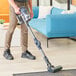 A man using a Lavex Pro cordless stick vacuum to clean a carpet.
