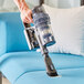 A hand using a Lavex Pro cordless stick vacuum to clean a blue couch.