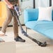 A man using a Lavex Pro cordless stick vacuum to clean a blue couch.