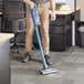 A man using a Lavex blue cordless stick vacuum to clean an office floor.