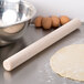 A maple wood French rolling pin and dough on a table.