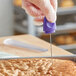 A gloved hand using a purple Choice cake tester to check a brown cake.