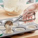 A person using a Choice stainless steel squeeze handle disher to scoop dough into a muffin tin.
