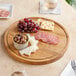 A Boska large round oak serving board with cheese, grapes, meat, crackers, and olives.