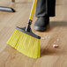 A person sweeping the floor with a yellow Lavex angled broom.