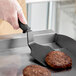 A hand using a Fourt&#233; black nylon spatula to flip burgers on a grill.